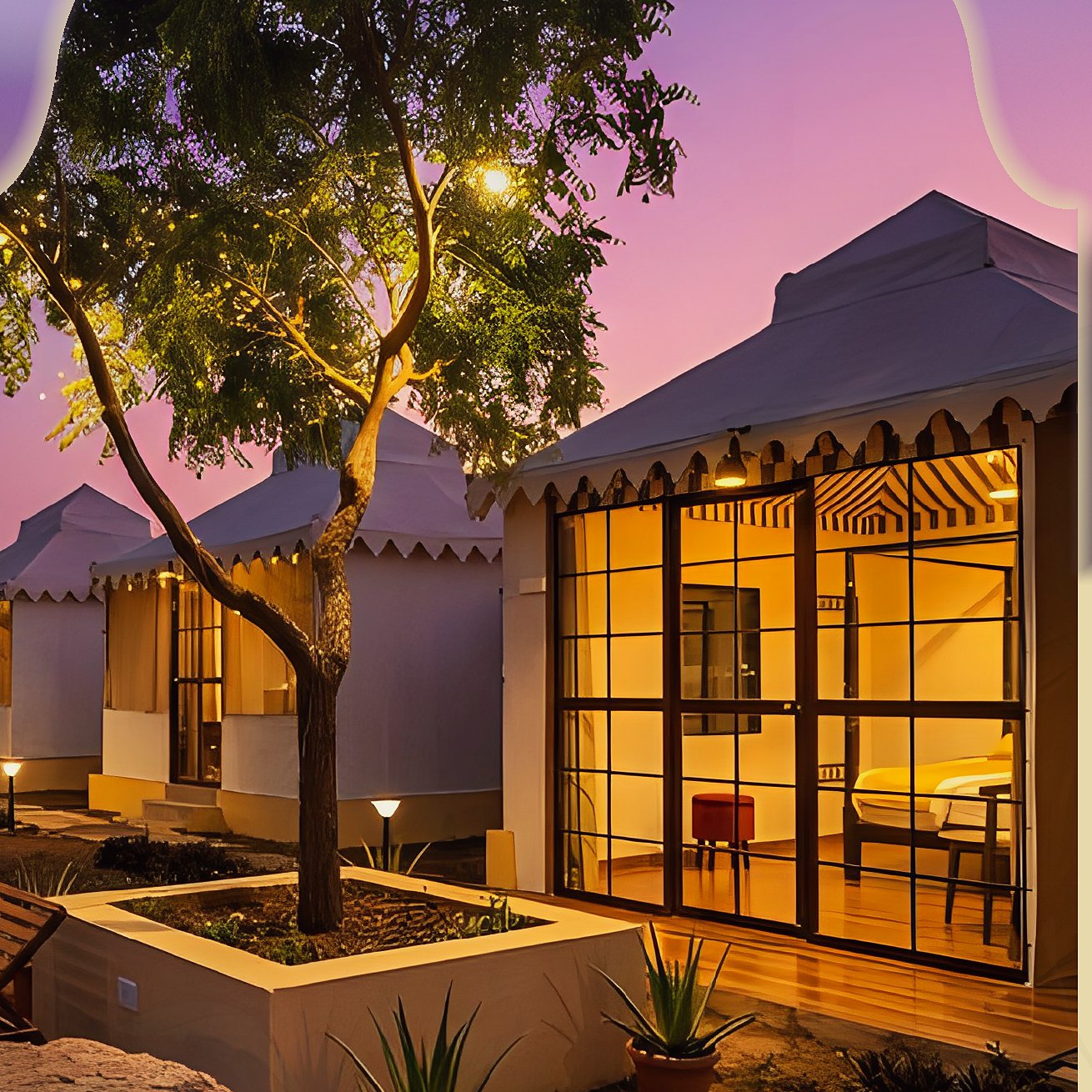 Cottages glowing at dusk beneath a tree strung with lights at The Majestic Heritage, Sasan Gir